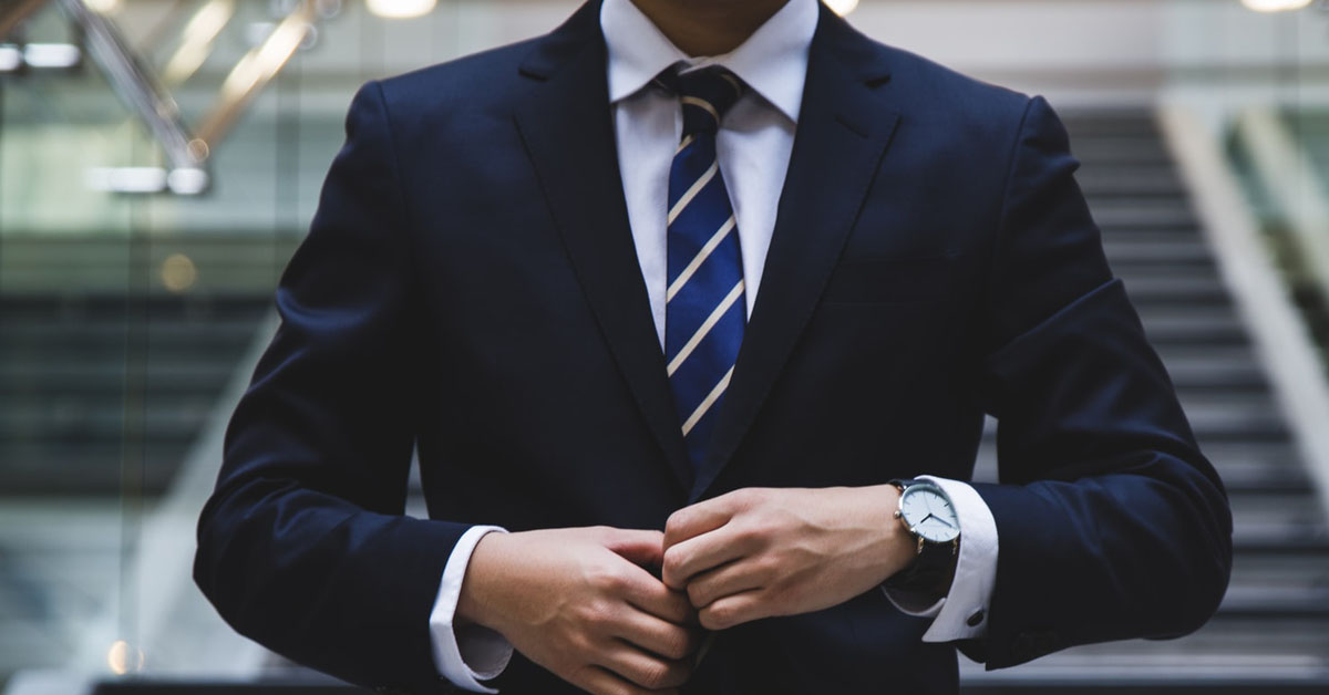 Businessman in navy suit with hands together closing his jacket button
